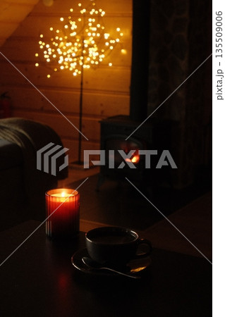 Cozy interior scene with warm candlelight, coffee cup, and glowing decorative tree lights 135509006