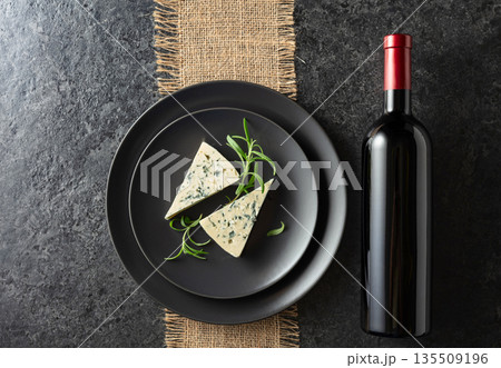 Bottle of red wine and blue cheese on a black plate. 135509196