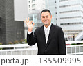 ビルを背景にOKをサインするスーツ姿の中年のアジア人のビジネスマン 135509995