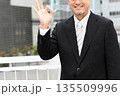 ビルを背景にOKをサインするスーツ姿の中年のアジア人のビジネスマン 135509996