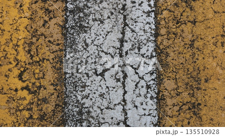 Vertical yellow and white stripe of painted asphalt with cracked rough texture, fragment of marked pedestrian crossing on road or highway in two colors, road background texture 135510928