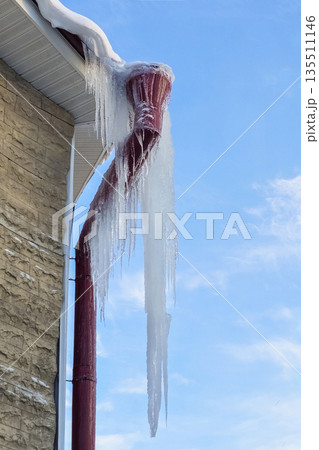 A dangerous icicle is hanging from the roof. 135511146