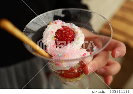 いちごとホイップクリームの春色パフェを持つ手元のクローズアップ 135511151