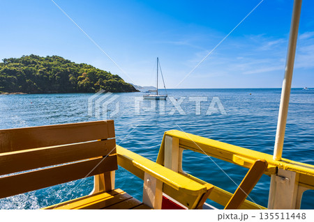 View from a ferry deck of a white sailboat anchored in the calm blue bay of Koh Samed, Rayong, Thailand 135511448