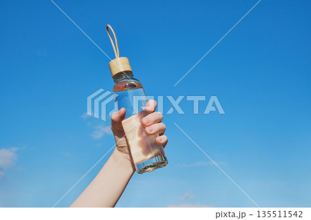 Hand holding reusable glass water bottle with water for hydration and sustainability 135511542