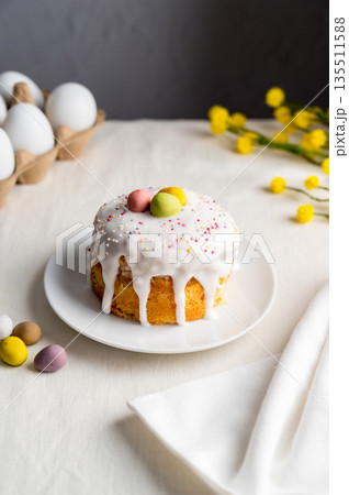 Easter festive cake with icing, sprinkles and eggs candy. White egg and spring, yellow flower twigs. Easter festive cake with icing, sprinkles and eggs candy. White egg and spring, yellow flower twigs. 135511588