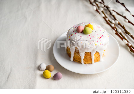 Easter festive cake with icing, sprinkles and eggs candy. White eggs and willow twigs. Copy space 135511589