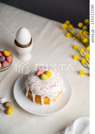 Easter festive cake with icing, sprinkles and eggs candy. White eggs and spring, yellow flower twigs. 135511590