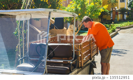 A man loads things into the back of a small electric car near his home A man loads things into the back of a small electric car near his home 135512951