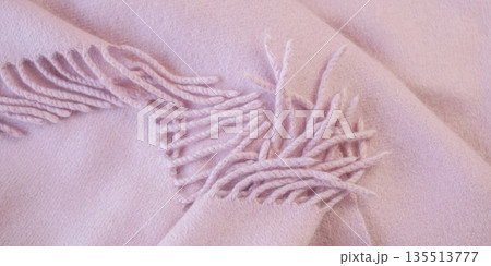 Pale pink cashmere scarf with fringe around the edge. Soft pink draped fabric texture. 135513777