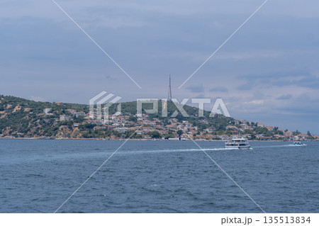 A picturesque view of Prince Islands showcases a boat gliding through tranquil waters, surrounded by lush greenery and quaint homes under overcast skies. A picturesque view of Prince Islands showcases a boat gliding through tranquil waters, surrounded by lush greenery and quaint homes under overcast skies. 135513834