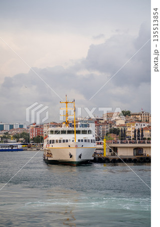 A ferry is moored at a dock along the Bosphorus, with urban buildings in the background under a cloudy sky, creating a tranquil atmosphere. A ferry is moored at a dock along the Bosphorus, with urban buildings in the background under a cloudy sky, creating a tranquil atmosphere. 135513854