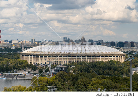 A stunning view of Luzhniki Park featuring Moscow City skyscrapers in the background, framed by vibrant greenery and dynamic cloud patterns. 135513861
