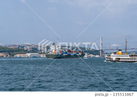 Cargo ships navigate the Bosphorus strait while a ferry crosses the water, with the city skyline visible in the background under clear skies. Cargo ships navigate the Bosphorus strait while a ferry crosses the water, with the city skyline visible in the background under clear skies. 135513867