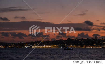 Colorful sunset paints the sky as a ferry navigates the Bosphorus, with city lights twinkling in the background and clouds reflecting the evening hues. Colorful sunset paints the sky as a ferry navigates the Bosphorus, with city lights twinkling in the background and clouds reflecting the evening hues. 135513886