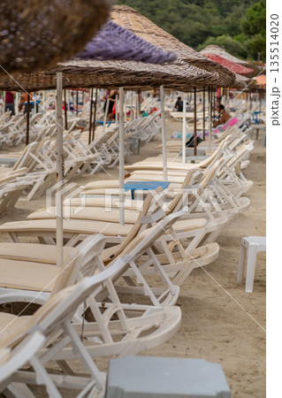 Sandy beach on Prince Islands features empty lounge chairs and colorful umbrellas under the sun, inviting visitors to unwind and enjoy the surroundings. 135514020