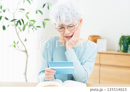 預金通帳を見て考えるシニア女性 135514023