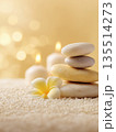 A collection of smooth stones and a flower sit on a textured surface with candles providing soft light in a wellness-focused setting. 135514273