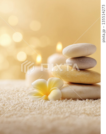 A collection of smooth stones and a flower sit on a textured surface with candles providing soft light in a wellness-focused setting. 135514273