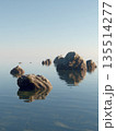 Rocks stand in still water, showing reflections while the open space and stone texture create a balanced scene under clear skies. 135514277