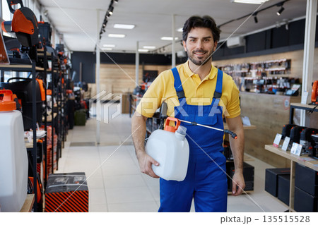 A man worker dressed in overalls is holding a sprayer in a store 135515528