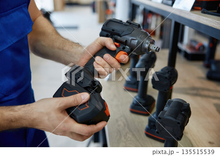 A man is holding a black and orange handheld drill in both hands 135515539