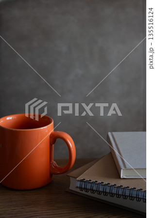 Orange cup with notes on table. Stack of notepads with a tea cup on beige background. Writing pads and mug. Writer interior. Cozy home. Orange cup with notes on table. Stack of notepads with a tea cup on beige background. Writing pads and mug. Writer interior. Cozy home. 135516124