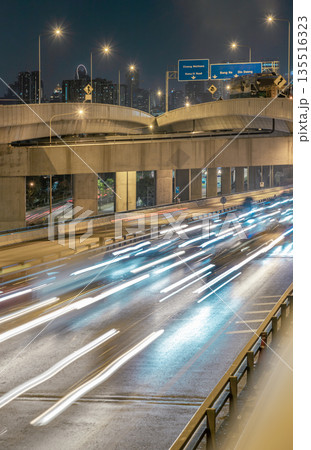 A nightscape view with bright glowing light trails effect of many cars headlights and rear lights on urban expressway. 135516323