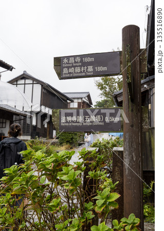 雨の日の馬籠宿に立つ観光案内標識と歴史的な街並み風景 135516890