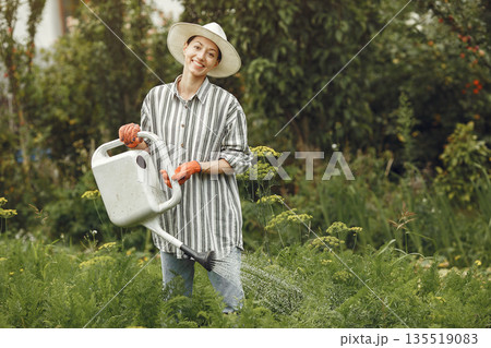 Gardening in summer. Woman watering flowers with a watering can. Girl wearing a hat. Gardening in summer. Woman watering flowers with a watering can. Girl wearing a hat. 135519083