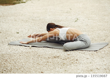 Pretty lady training on a summer beach. Brunette doing yoga. Girl in a sportsuit. 135519087