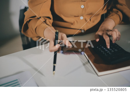 Business woman using calculator to calculate financial report, working at office with laptop computer on table. Asian female accountant or banker making calculations. finances and economy concept Business woman using calculator to calculate financial report, working at office with laptop computer on table. Asian female accountant or banker making calculations. finances and economy concept 135520805