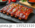 Close-up of juicy fresh grilled glazed pork ribs on black slate board with ketchup and spices 135521310