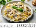 Close-up of delicious vegetarian pasta pappardelle dish with mushrooms and white creamy sauce served on grey plate with fresh basil on concrete background 135521315