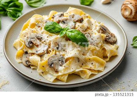 Close-up of delicious vegetarian pasta pappardelle dish with mushrooms and white creamy sauce served on grey plate with fresh basil on concrete background 135521315
