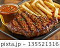 Closeup of juicy grilled cowboy butter steak served with golden fries and red dipping sauce on black plate on wooden table 135521316