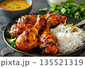 Close-up of several grilled, smoking tandoori chicken legs marinated with tandoori masala spices with curry basmati rice on black plate on dark background, popular traditional Indian dish 135521319