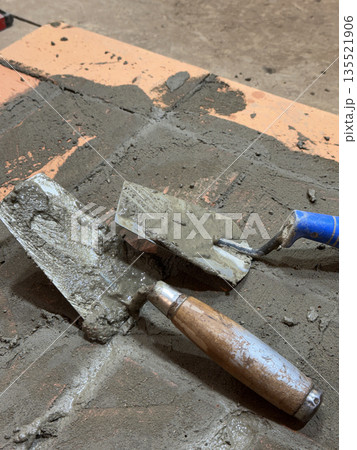 Two trowels on the brickwork of a heating stove base. Close-up. Two trowels on the brickwork of a heating stove base. Close-up. 135521906