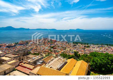 Panoramic top view of Naples rooftops from Castel Sant Elmo, with the sea in the distance and Mount Vesuvius rising above the city on a clear summer day. 135522093