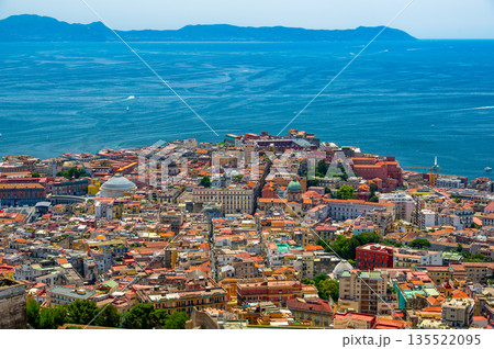 Panoramic top view of Naples rooftops from Castel Sant Elmo, with the sea in the distance and Mount Vesuvius rising above the city on a clear summer day. 135522095