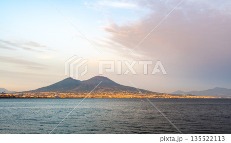 Panoramic view of Mount Vesuvius rising above the city of Naples, Italy, under a clear blue sky, showing the dramatic contrast between urban life and the famous volcano. 135522113