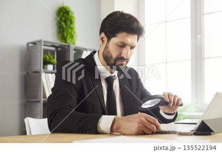 Closeup of businessman auditing paperwork and reviewing data with magnifier 135522194