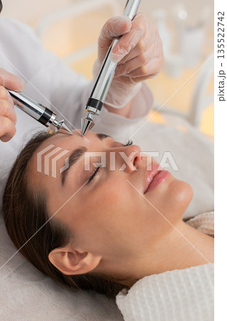 Beautician doctor makes woman micro currents face therapy using electrical impulses in spa salon 135522742