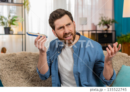 Young man carefully listening to voice message on smartphone, tilting head, focusing to hear clearly Young man carefully listening to voice message on smartphone, tilting head, focusing to hear clearly 135522745