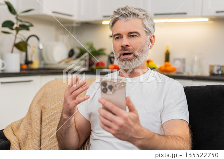 Middle-aged man practices language phrases with headphones on smartphone app repeats and feels proud Middle-aged man practices language phrases with headphones on smartphone app repeats and feels proud 135522750