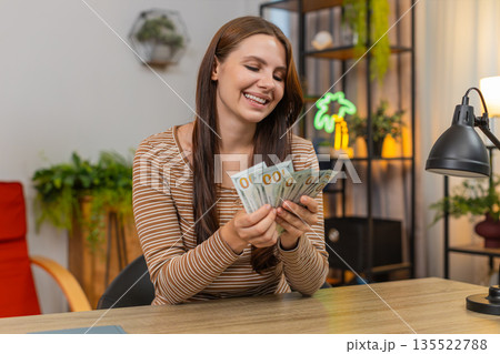 Woman counts cash dollar bills money at table smiles pleased about salary lottery win savings income Woman counts cash dollar bills money at table smiles pleased about salary lottery win savings income 135522788