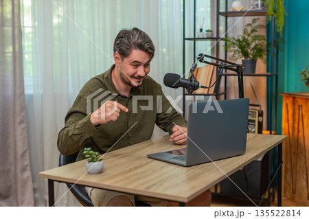 Middle-aged man hosting live vlog speaking to laptop microphone engaging interaction at table desk Middle-aged man hosting live vlog speaking to laptop microphone engaging interaction at table desk 135522814