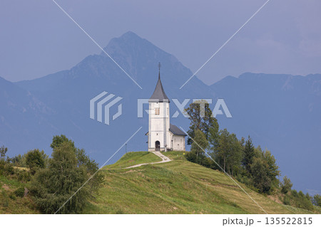 Jamnik, Slovenia. The Jamnik Church is a charming 15th-century chapel in the Kamnik-Savinja Alps near Kranj, breathtaking views of the surrounding mountainous landscape. The Church of St. Primoz Jamnik, Slovenia. The Jamnik Church is a charming 15th-century chapel in the Kamnik-Savinja Alps near Kranj, breathtaking views of the surrounding mountainous landscape. The Church of St. Primoz 135522815
