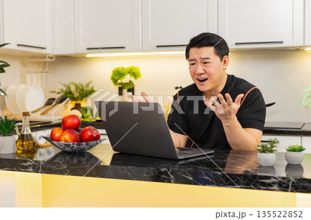Upset Asian man reacts to bad online casino loss while reading laptop screen at home kitchen indoors Upset Asian man reacts to bad online casino loss while reading laptop screen at home kitchen indoors 135522852