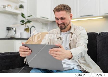 Young man freelancer celebrates project success on laptop reads news laughs and makes victory sign 135522854